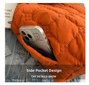Detail view of the side hidden zipper pocket on orange quilted tote bag holding a phone