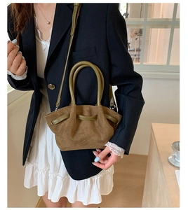 Detail of a brown suede bucket bag featuring green leather handles and pleated design
