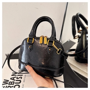 Detail of black mini shell bag with glossy crinkle texture and gold metal zippers