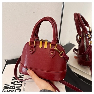 Detail of burgundy shell bag showing wine red leather texture and gold zipper hardware