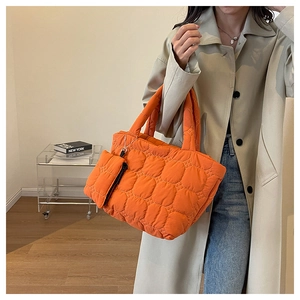 Quilted orange tote bag with matching pouch charm shown on a stylish trench coat