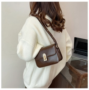 Dettaglio della borsa a tracolla retrò marrone con chiusura dorata su un maglione bianco