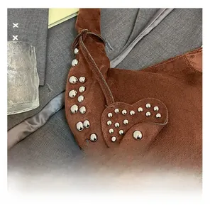 Détails de rivets argentés sur cabas en daim marron avec breloque cœur et style punk