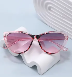 Pink cat eye sunglasses with tortoise pattern on a white wavy stand with blue background