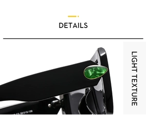 Detail of black sunglasses featuring a green gemstone inlay and golden textured hinge