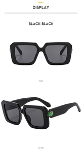 Detail of black square sunglasses featuring green gemstone accents on the side temples