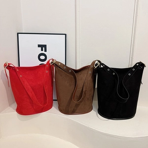 Three suede bucket bags in red, brown, and black featuring metal eyelet side details