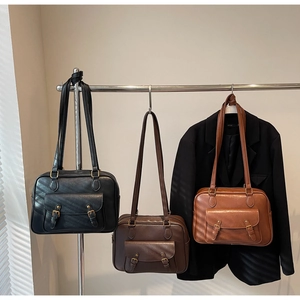 Three vintage leather messenger bags in black, coffee, and brown colors hung on a metal rack