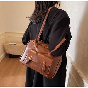 Detail view of the brown vintage briefcase style shoulder bag worn by a model