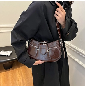 Close-up of a dark brown crescent shoulder bag featuring vintage buckles and zippers