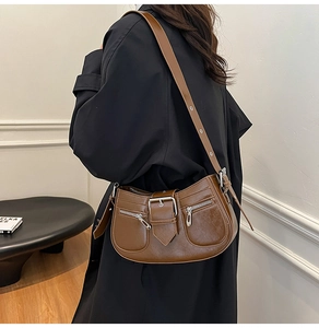 Close-up of brown glossy leather crescent shoulder bag with silver buckle and zippers