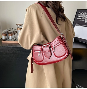 Side view of dark red patent leather shoulder bag with silver zippers and buckle strap