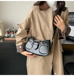 Detail of black glossy crescent saddle bag with silver zippers and metal buckle strap