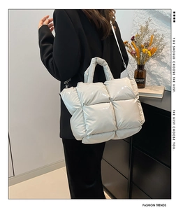 Quilted puffer tote bag in light grey with silver hardware worn by model in black blazer