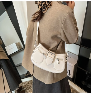 Detail view of cream leather shoulder bag featuring dual decorative zippers and metal buckle
