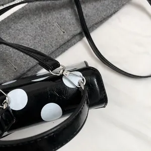 Close-up of silver metal hooks and detachable strap on black polka dot leather bag