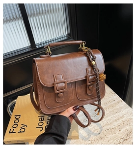 Close-up of vintage brown leather satchel with dual buckle straps and woven bag charm