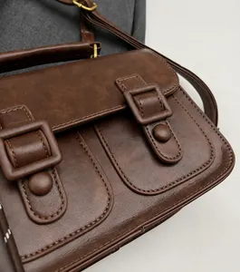 Detail of dark brown vintage faux leather texture and bronze buckles on satchel bag