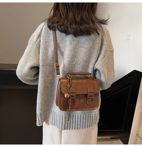 Brown vintage satchel with twin front pockets and decorative bell charms on the strap