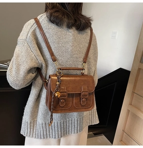 Brown vintage satchel showing the double strap detail and side bell charm on back