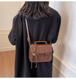 Detail view of a vintage brown leather crossbody bag with decorative buckles and top handle