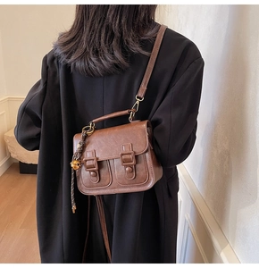 Retro brown leather crossbody bag with top handle and gold bell charm on a model