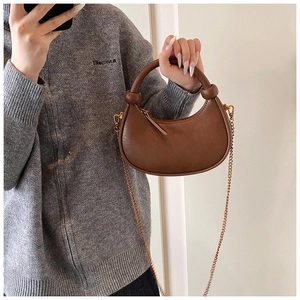 Detailed shot of brown crescent bag with knotted handle and fine gold metal chain strap