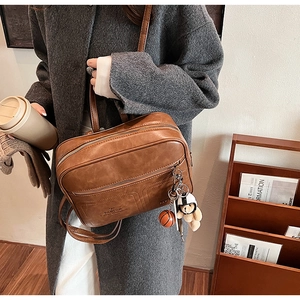 Detail of vintage brown leather backpack featuring a plush bear charm and embossed logo