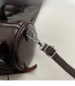 Détail du sac cylindre marron foncé brillant avec ferrures argentées et boucles réglables