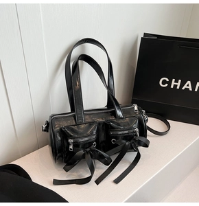 Détail d'un sac polochon noir brillant avec nœuds décoratifs et poches zippées multiples