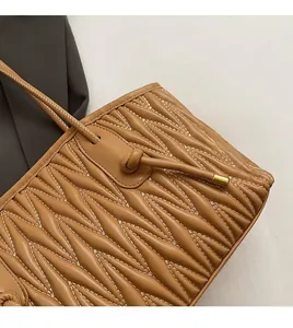 Detail of wave quilted brown leather shoulder bag with drawstring knot and gold hardware