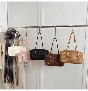 Close-up of pleated leather tote bags in five colors hanging on a metal rack