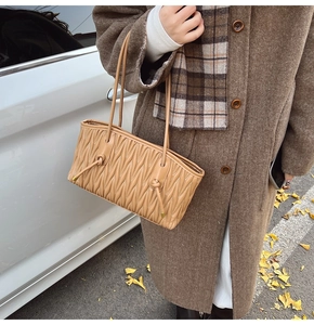 Detail of khaki pleated tote bag with wave quilting and knot accents for winter style