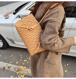 Detail of caramel pleated matelassé shoulder bag with side knot drawstrings and strap