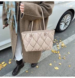 Quilted tote bag in light beige with diamond stitching carried by a woman in a brown coat