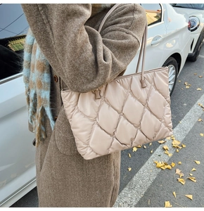Detail view of a beige quilted tote bag worn with a winter coat in an outdoor street setting