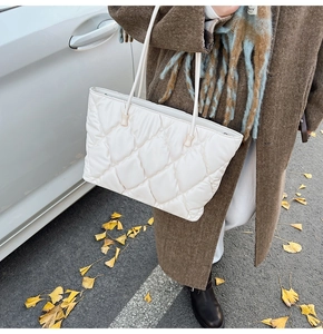 Close-up of white quilted tote bag with large diamond stitching worn in an outdoor city setting