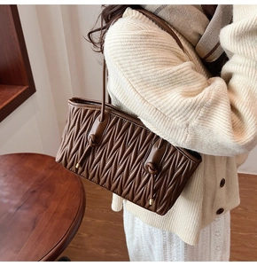 Detail of dark brown quilted shoulder bag with wave texture and gold metal accents