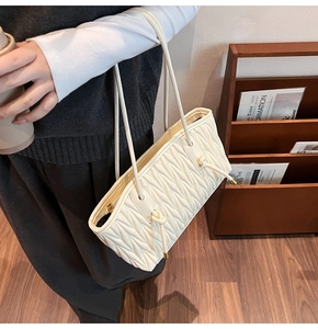 Detail showing beige matelassé pleated texture and knotted straps on a leather tote