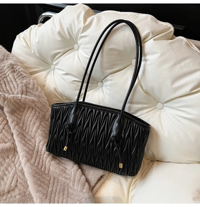 Detail of black matelassé pleated shoulder bag with gold-tipped drawstrings on white leather