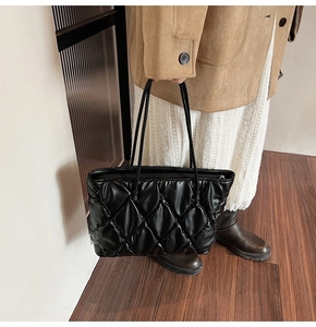 Close-up of black quilted tote bag with diamond stitching and slim shoulder straps