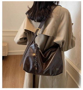 Detail of deep brown glossy leather tote bag with wide strap and gold metal ball charm