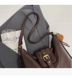 Detail of dark brown leather tote with golden buckle and cute brown bear keychain charm