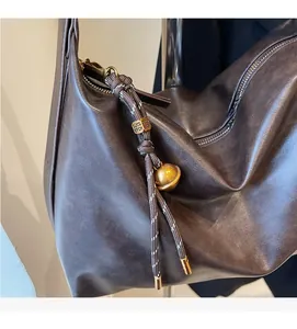 Detail of dark brown leather hobo bag with gold hardware and woven rope pendant