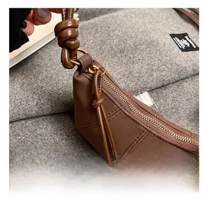 Close-up of golden zipper and knotted leather strap on brown quilted baguette bag