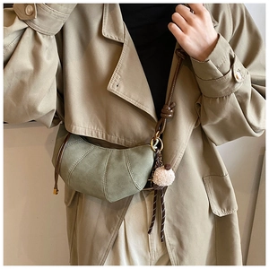 Detail of sage green suede half-moon bag with vertical stitching and plush ball charm