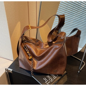 Detailed mirror shot of a vintage coffee leather tote bag with braided charm and gold hardware