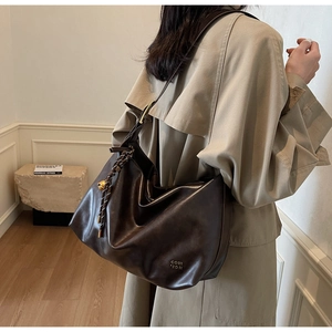 Détail du sac hobo marron foncé avec breloque cloche tressée et texture de cuir souple