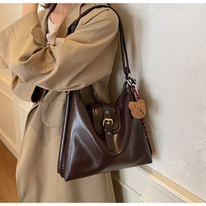 Detail of deep brown leather tote bag with gold buckle and plush bear pendant accessory