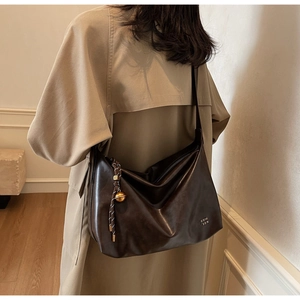 Détail du sac cabas en cuir brillant marron avec breloque dorée et logo métallique